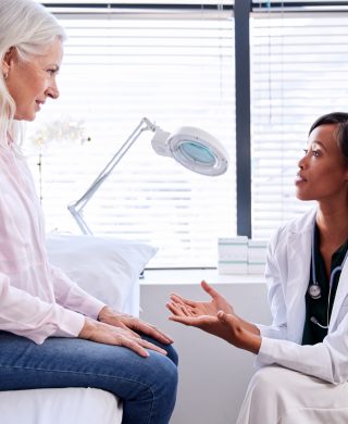 Mature woman in consultation with female doctor sitting on examination table, used to explain dense breast tissue