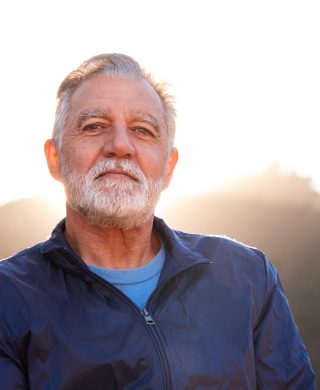 Older man photographed with bright natural light behind him, used to explain symptoms of an enlarged prostate