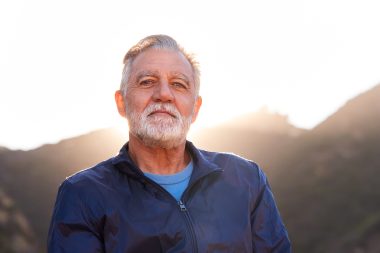 Older man photographed with bright natural light behind him, used to explain symptoms of an enlarged prostate