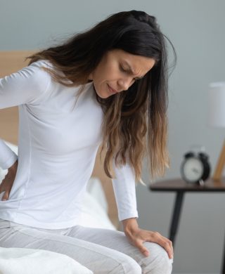 Woman looking unhappy and holding her lower back, used to explain endometriosis and pcos and uterine fibroids