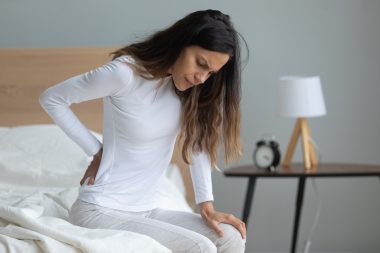 Woman looking unhappy and holding her lower back, used to explain endometriosis and pcos and uterine fibroids