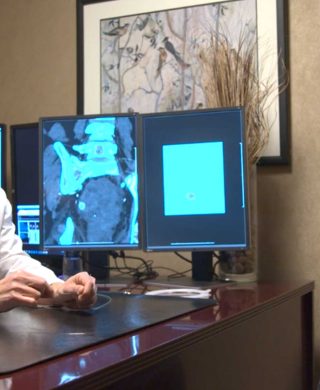 Dr. Eric Wang from Charlotte Radiology looking on a computer screen, used to explain the vascular embolization procedure he uses.