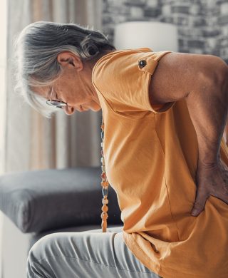 A woman holding her lower back with her hands, used to explain spinal compression fracture