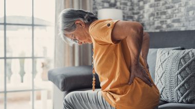 A woman holding her lower back with her hands, used to explain spinal compression fracture