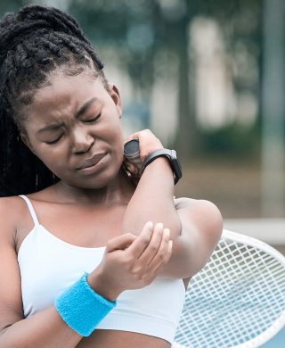 Young tennis player holding her elbow, used to explain sports injuries