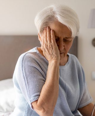 Older woman holding the side of her forehead with her hand, used to explain reasons why someone may need a head CT