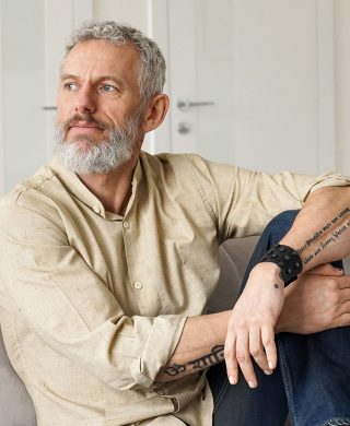 Gentleman with a white beard and hair sitting with his arms crossed over one leg and looking off camera, used to explain enlarged prostate treatment