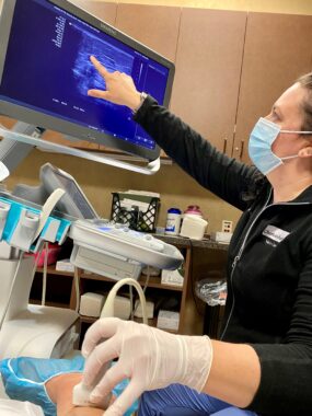 A vein specialist pointing to a monitor in a medical office