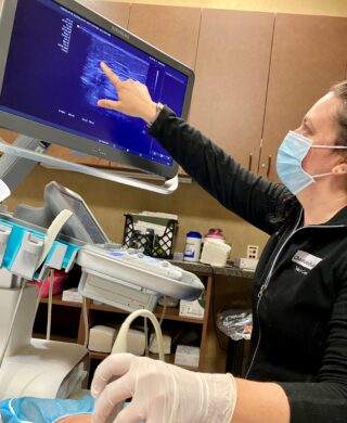 A vein specialist pointing to a monitor in a medical office