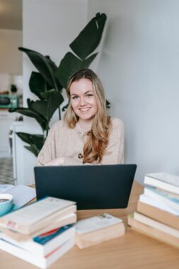 A young blond haired woman sitting in front of a laptop and smiling