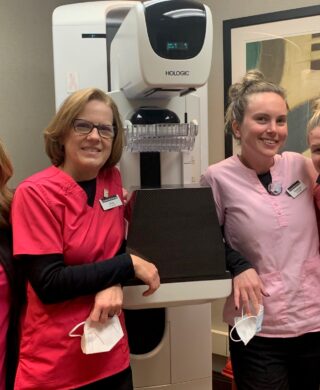 A group of breast health specialists at Charlotte Radiology in uniforms and standing in front of a mammography machine