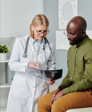 Medical provider in a white coat shows a young Black male patient medical scan results to help encourage preventive health screenings