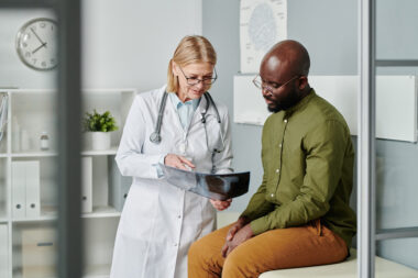 Medical provider in a white coat shows a young Black male patient medical scan results to help encourage preventive health screenings